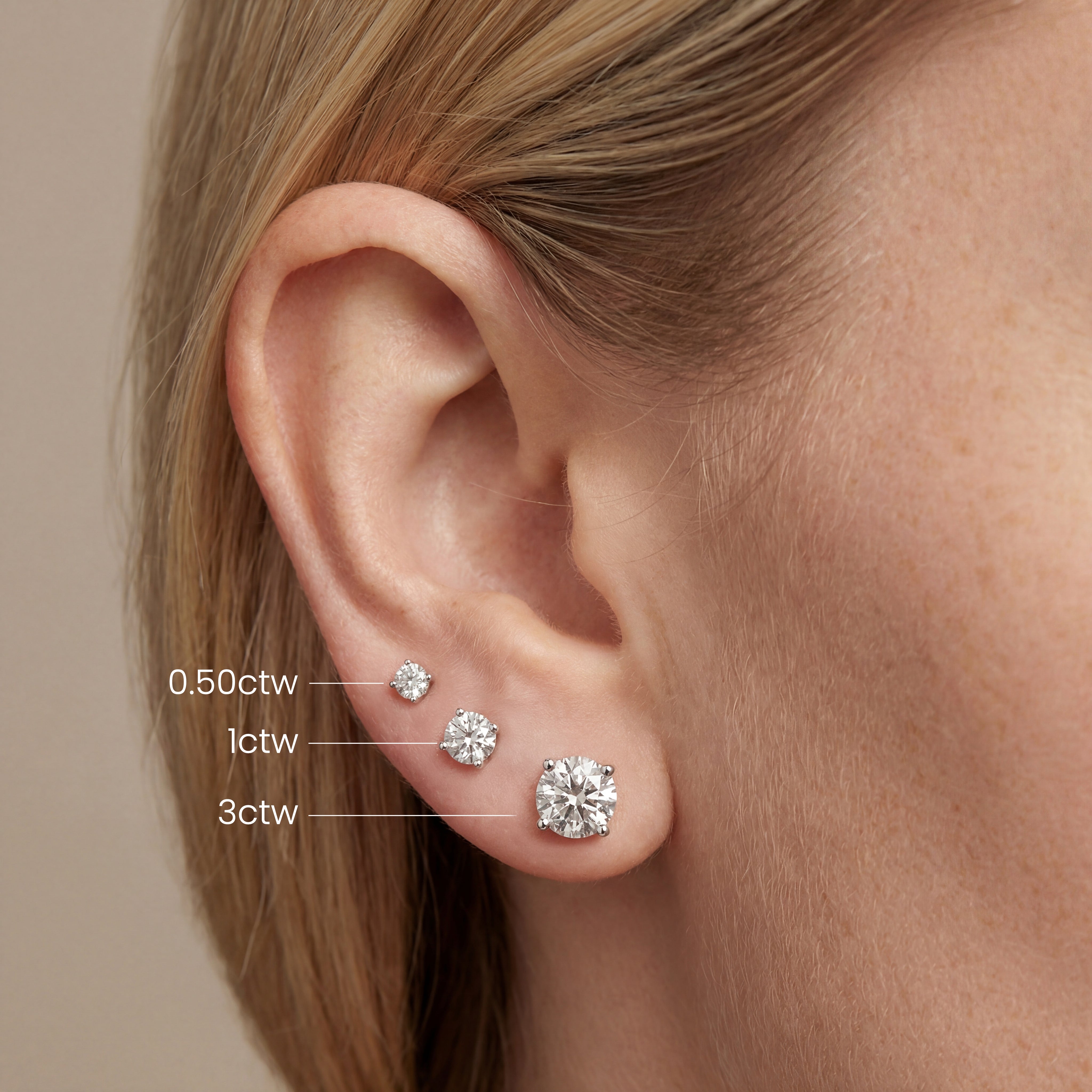 an ear with 0.50, 1, and 3 carat round lab grown diamond stud earrings, showing size comparison by Michael Gabriels