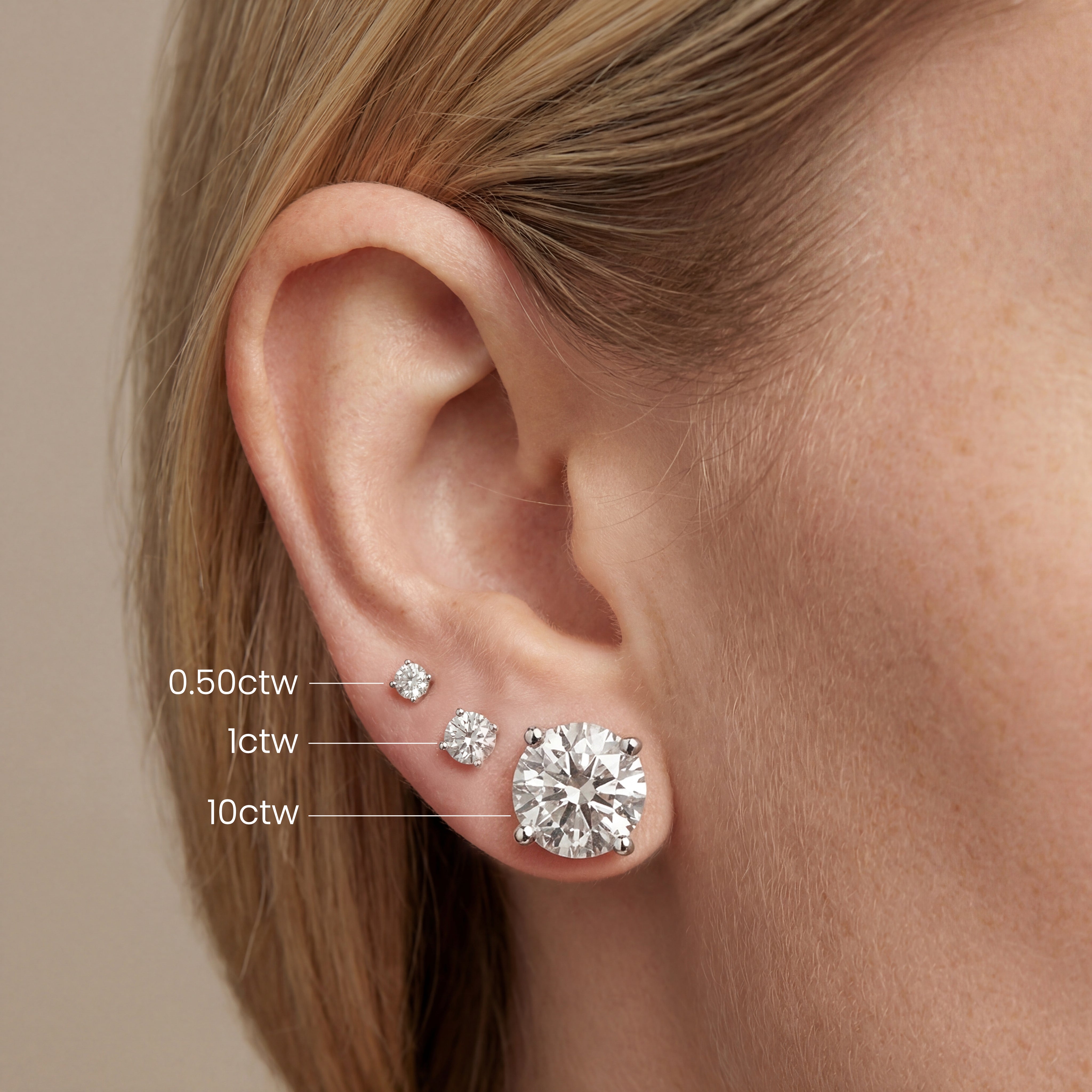 an ear with 0.50, 1, and 10 carat round lab grown diamond stud earrings, showing size comparison by Michael Gabriels
